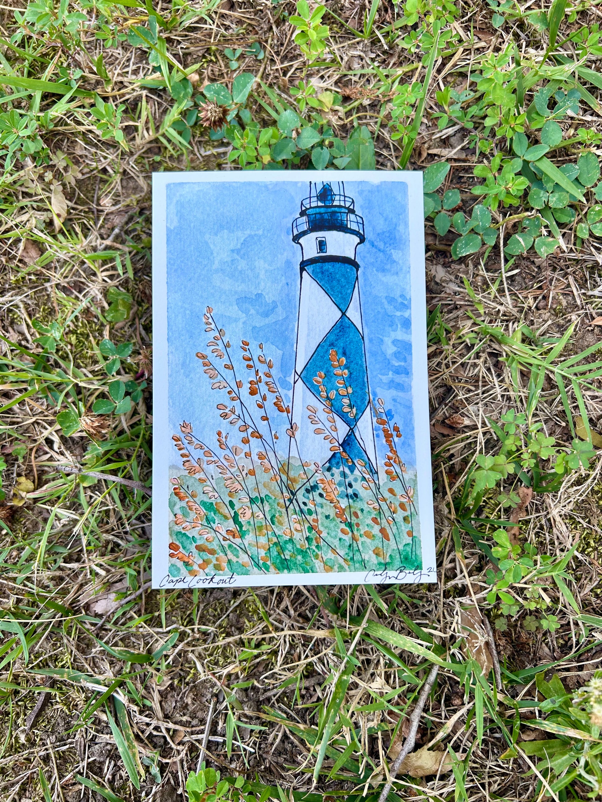 Blue and white lighthouse in the background under a blue sky with wildflowers.